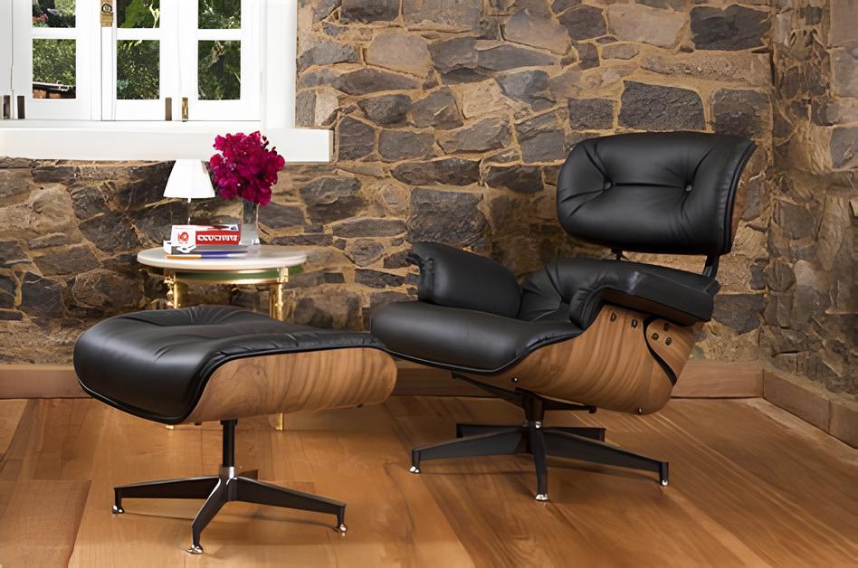 ambiente com uma poltrona e descaso para pés modelo charles eames de couro preto com marrom imitando madeira, ao lado uma mesinha redonda pequena com objetos decorativos , parede atrás toda de tijolos expostos