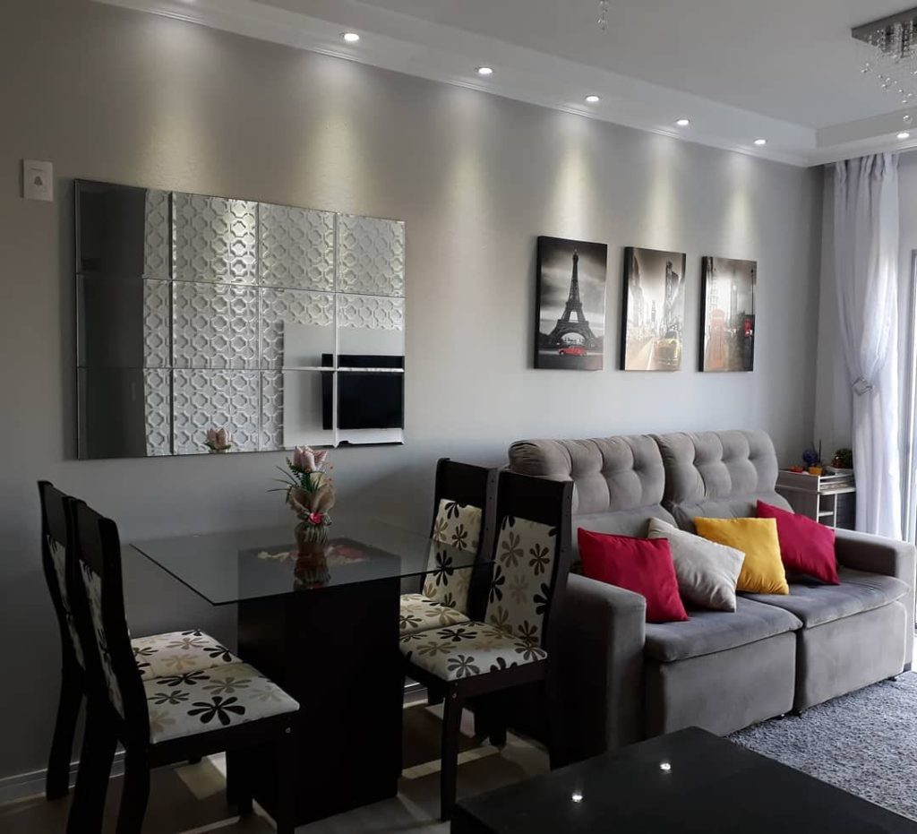 sala com uma mesa de 4 cadeiras, espelho medio na parede, sofa com 2 lugares cinza