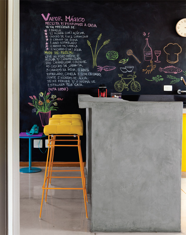 espaço com uma decoração na parede de lousa em tinta preta com bancada e duas cadeiras amarelas 