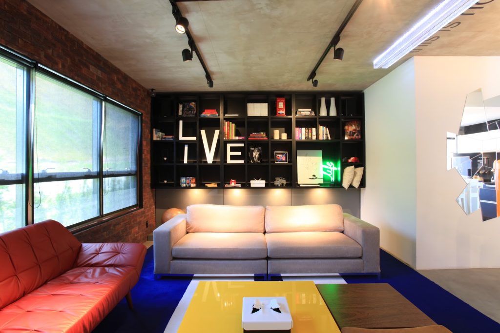 sala com estante grande em divisórias com uma luminária neon, 2 sofás de 2 e 3 lugares 