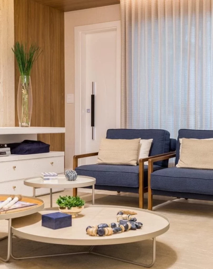 sala de estar com 2 poltronas azuis, 3 mesas de central na cor bege 