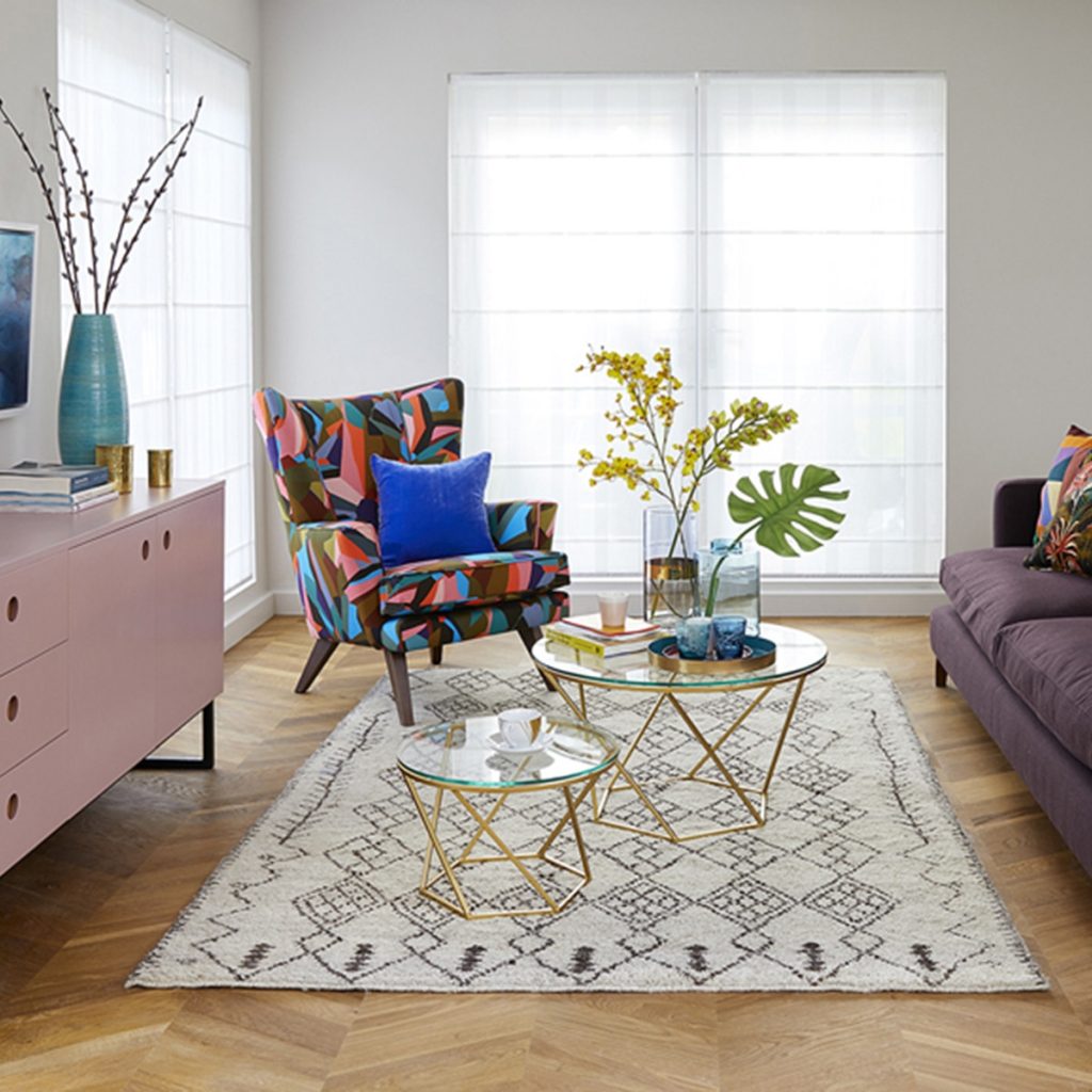 sala pequena com poltrona colorida, mesa de centro de vidro com objetos decorativos em cima 