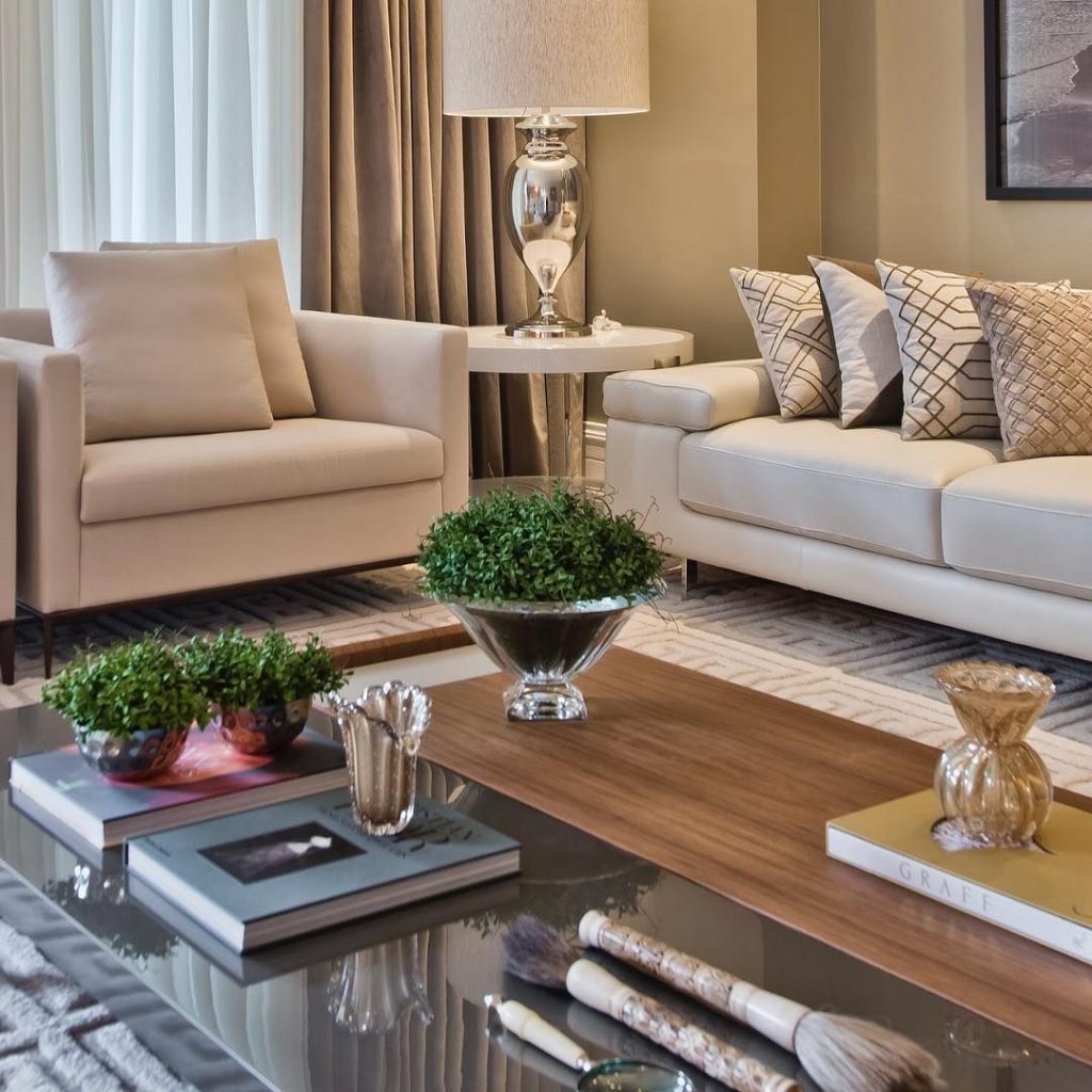 sala de estar com sofa e poltrona nas cores claras, com uma mesa de centro com plantas para decoração 