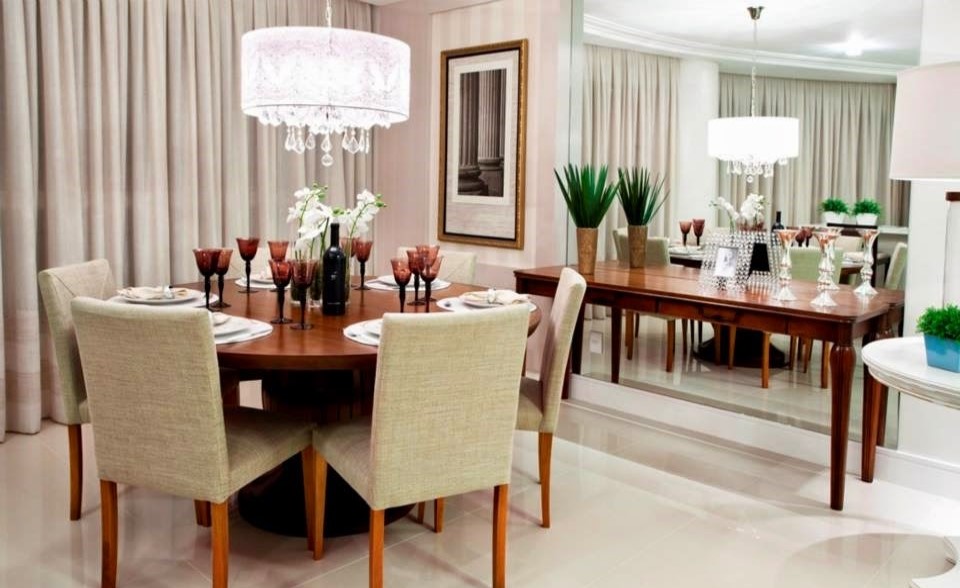 sala de jantar com mesa redonda na cor verniz, espelho grande na parede como decoração