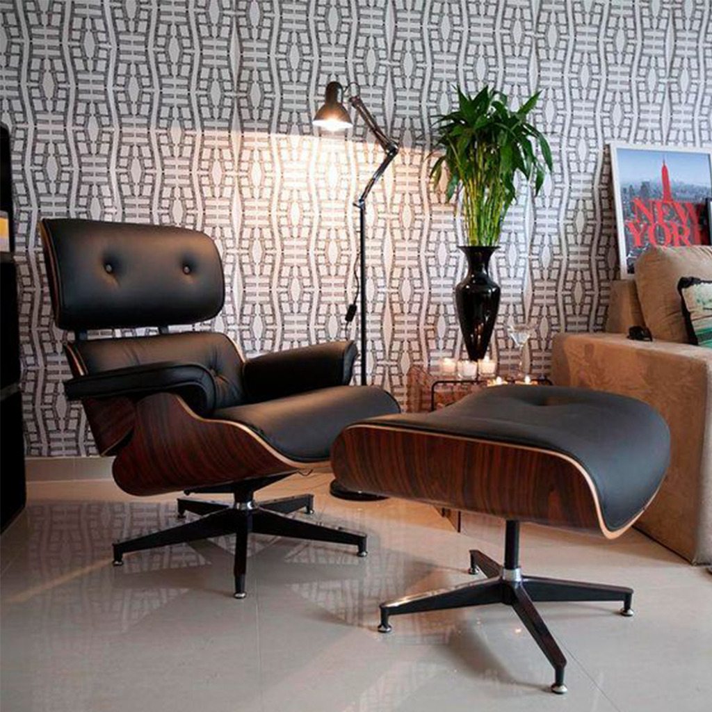 sala de tv com uma poltrona estilo charles eames de couro preto com detalhes em madeira, ao lado um sofa grande bege, e uma mesinha de vidro com vaso preto e planta