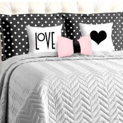 quarto do casal com cama grande e uma cabeceira na cor branca, duas almofadas grandes pretas de bolinhas brancas, em frente duas na cor branca com frases de love e outra desenho de um coração preto, edredom cinza