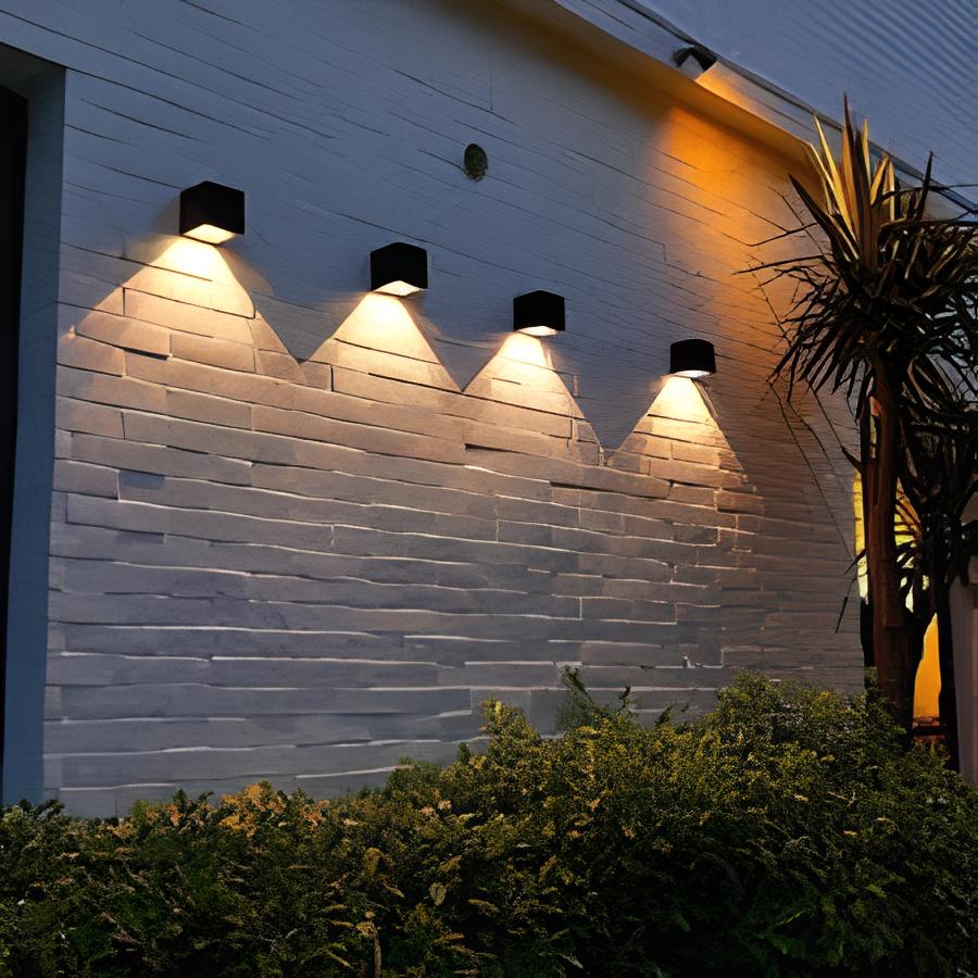 área externa de uma casa com luminárias na parede, plantas e árvores.