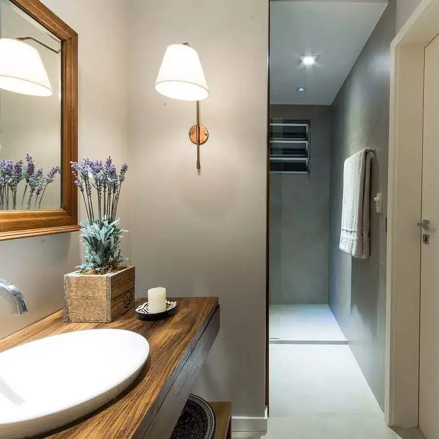 banheiro pequeno com pia, espelho e armário de madeira e uma luminária na parede ao lado.