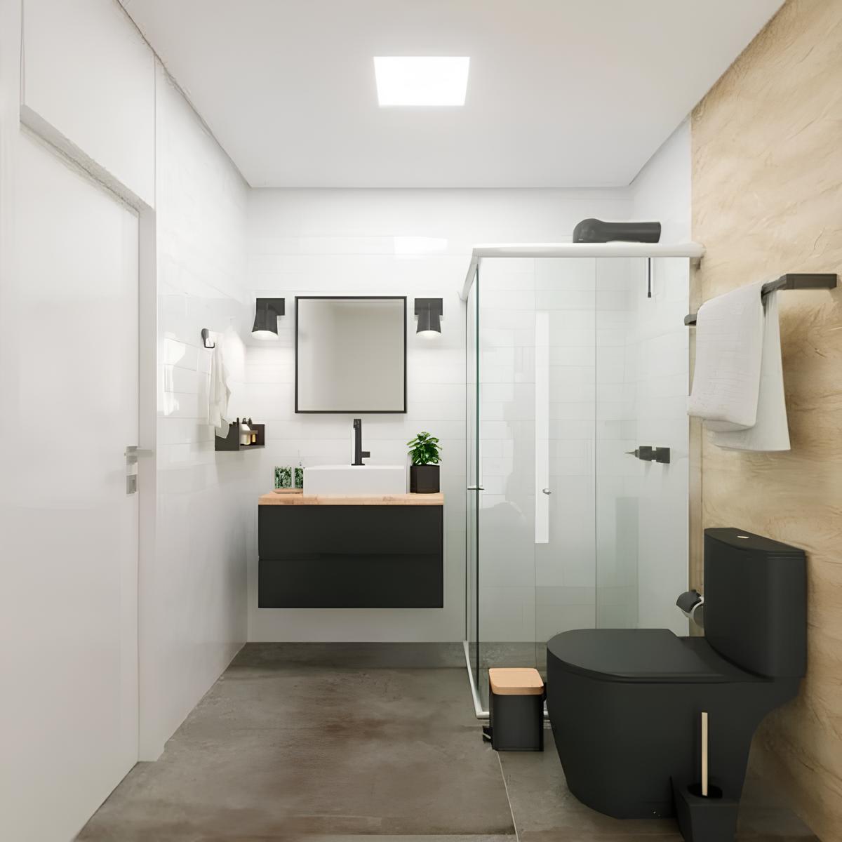 banheiro com arámrio e pia, um espelho, dois vasinhos de plantas decorativos em cima do armário, um box com chuveiro ao lado, e um vaso sanitário com caixa acoplada nas cores pretas, no teto um luminária embutida de LED.