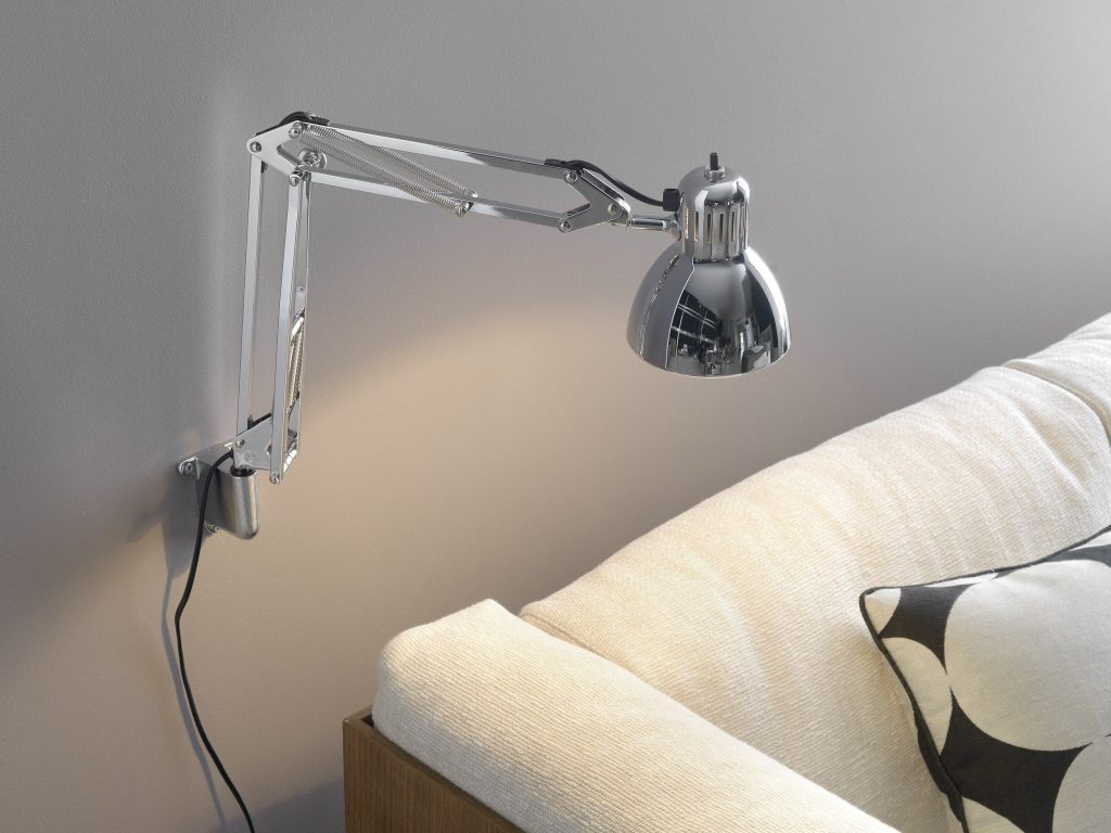ambiente com claro, almofadas, na parede atrás do sofá uma luminária de parede estilo braço articulado.