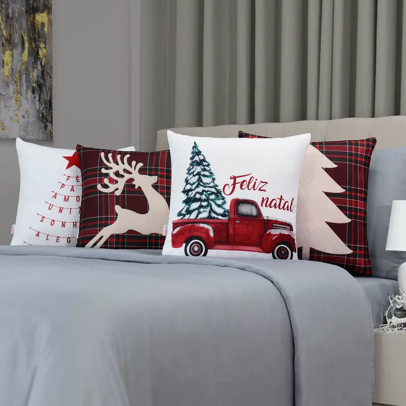 quarto com uma cama de casal com edredom cinza e em cima almofadas decorativas de natal, ao lado criado mudo com luminária e enfeite de natal.