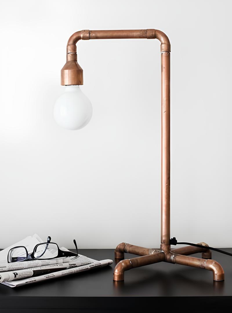 modelo de uma luminária feita de cano de PVC, ao lado dela um jornal e óculos de leitura.