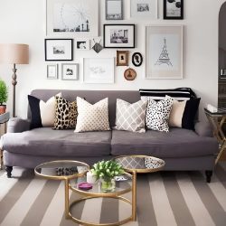 sala de estar com sofá cinza e varias almofadas em cima decorando, na parede atrás vários quadros pendurados, ao lado do sofá uma luminária.