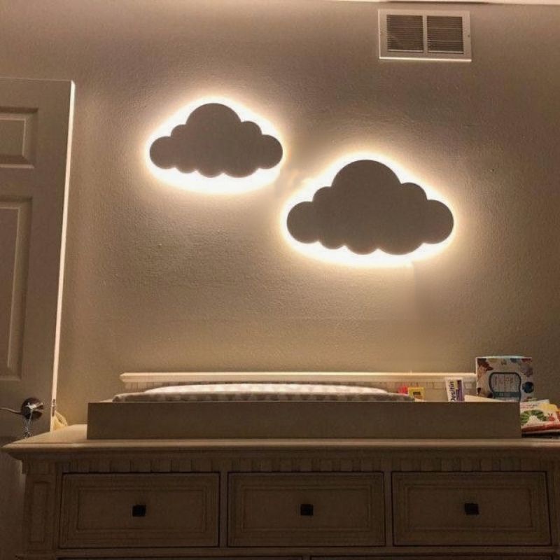um quarto infantil com luminárias de parede em formato de nuvem, com um trocador de fraldas em cima de um armário com gavetas.