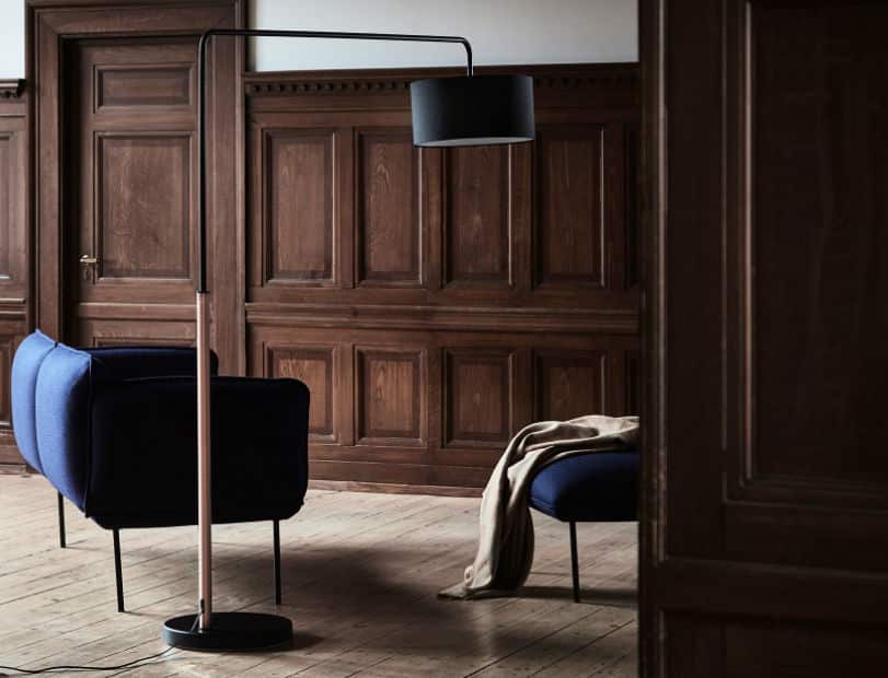 escritório estilo rústico com uma poltrona na cor azul escuro e uma descanso para pés na mesma cor da poltrona , ao lado da poltrona uma luminária alta de chão.