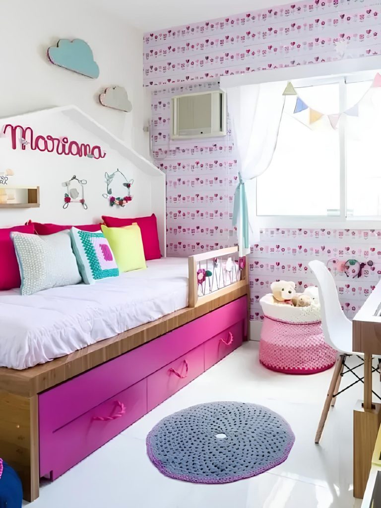 quarto infantil de menina com cama triliche, em cima almofadas infantis nas cores pink e branco, ao lado uma cesta de crochê com ursinhos dentro, ao lado uma mesinha de estudos.