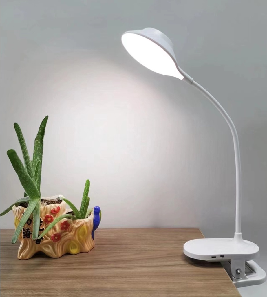uma mesa de madeira com uma luminária de grampo na cor branca flexível e ao lado dela um vasinho decorativo com cacto.