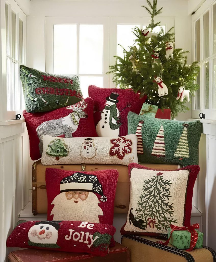 ambiente com várias almofadas natalinas em formatos e desenhos diferentes, atrás uma árvore com enfeites de natal.