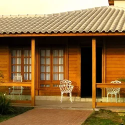 casa de madeira pré fabricada com dois quartos e uma varanda grande, nas laterias jardim com bastante árvores e plantas.