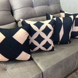 sofá na cor cinza com quatro almofadas em cima decoranto com formas geométricas e nas cores azul e rosa bebe.