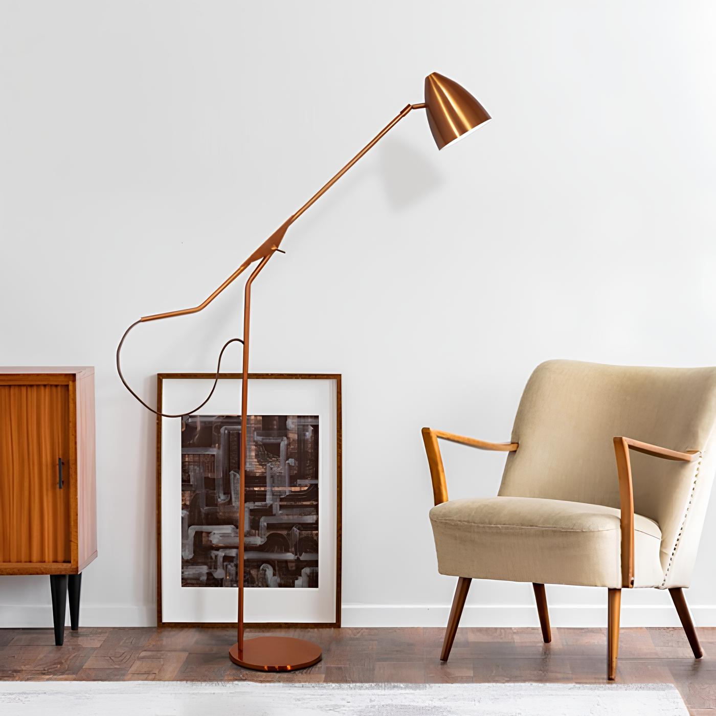 ambiente com uma poltrona com pés palito e estofamento bege, ao lado um quadro decorativo encostado na parede ao chão, em frente ele uma luminária de chão alta e uma armário de madeira.