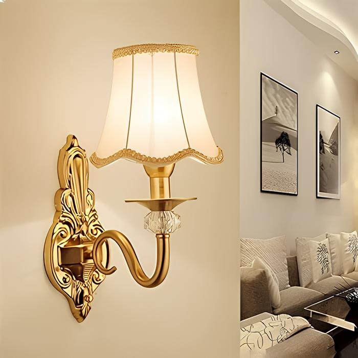 sala de estar com sofá e almofadas, na parede atrás do sofá quadros decorativos pendurados, na parede lateral uma luminária de parede em formato de abajur.