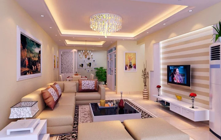 sala de estar ampla moderna com luminárias de teto e um lustre de cristal central, um sofá grande na cor bege com almofadas em cima, uma mesinha quadrada de centro, um painel com tv parede atrás do sofá com quadro decorativo.