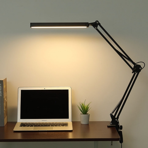 mesinha de trabalho com um notebook em cima, um vasinho pequeno de planta e uma luminária estilo grampo reclinável na cor preta.
