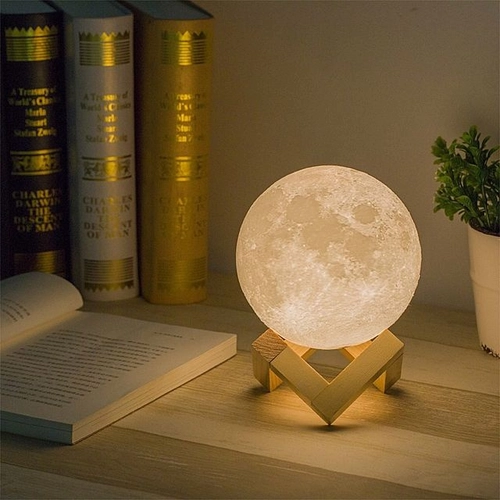mesinha me madeira com uma luminária em formato de lua, com alguns livros e objetos decorativos.