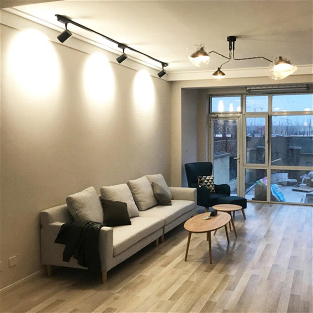 sala de estar de um apartamento com sofá, mesinha de centro de madeira com poltrona e descanso de pés ao lado. no teto luminárias de LED estilo de trilho.