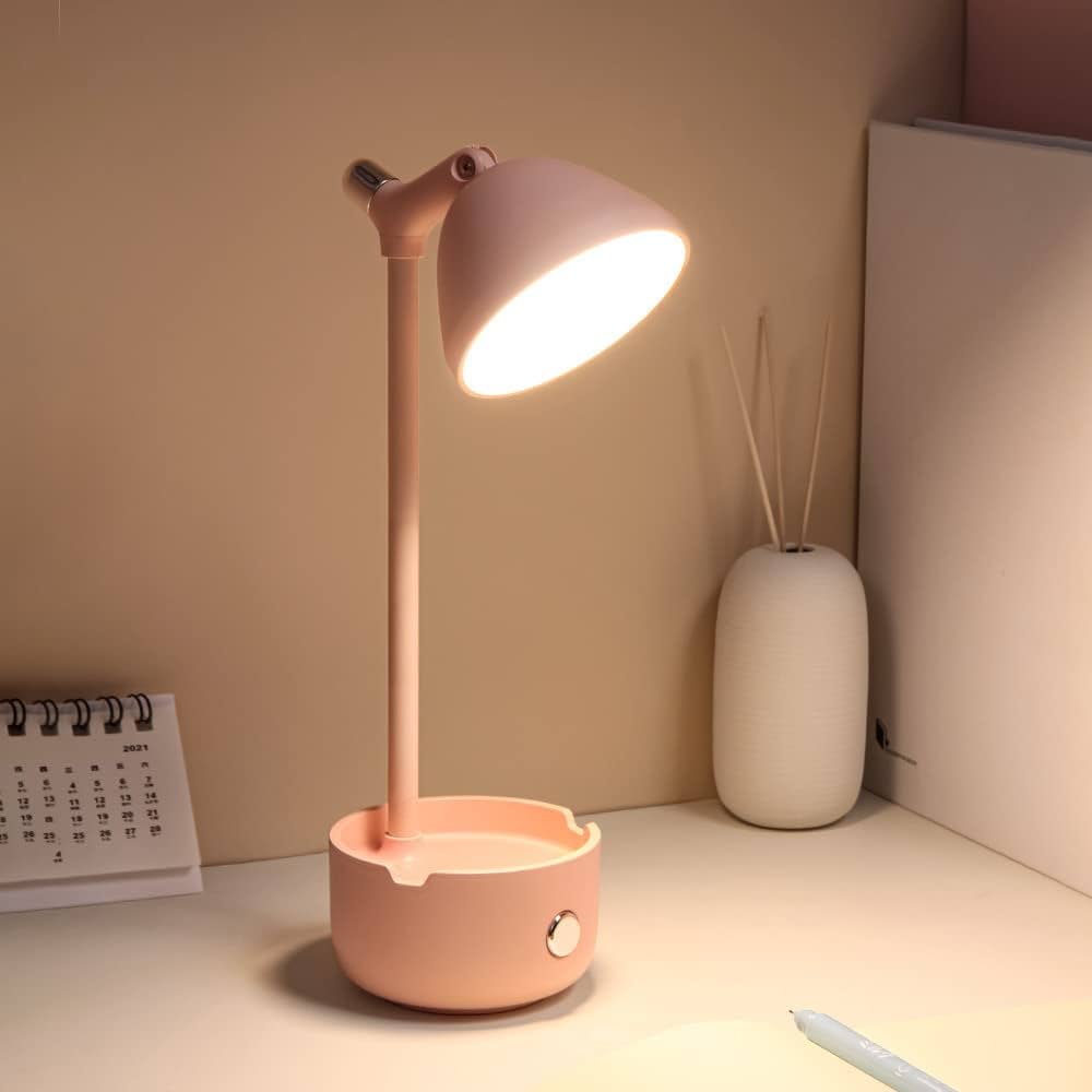 mesinha branca com uma luminária de Led na cor rosa bebe, ao fundo um difusor de cheiro com calendário ao lado,