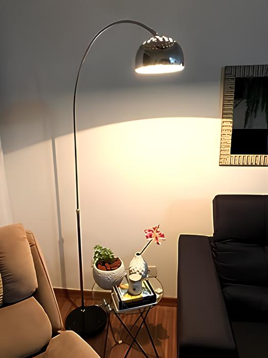 espaço com uma poltrona bege, um sofá preto, no meio deles uma mesinha de vidro redonda pequena com objetos decorativos e uma luminária alta  de metal.