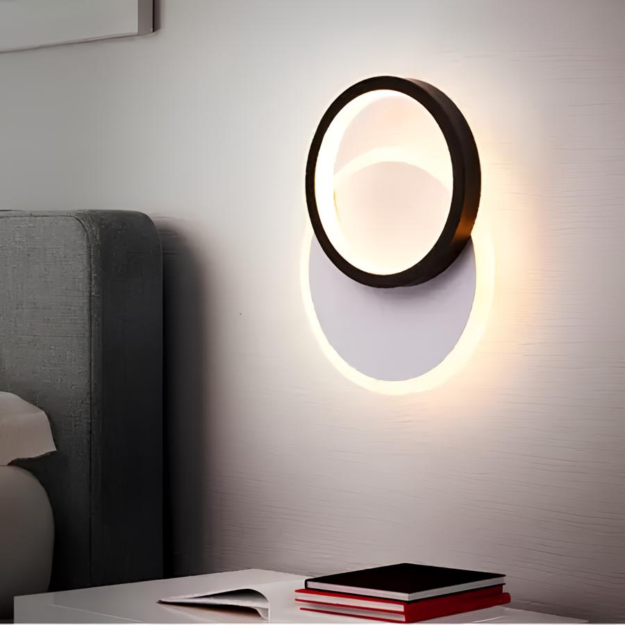 quarto com cama, criado mudo com livros em cima e na parede uma luminária de parede redonda de plafon.