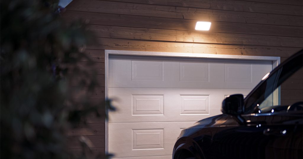 área externa de garagem com um carro para lado de fora e luminárias refletores por fora.