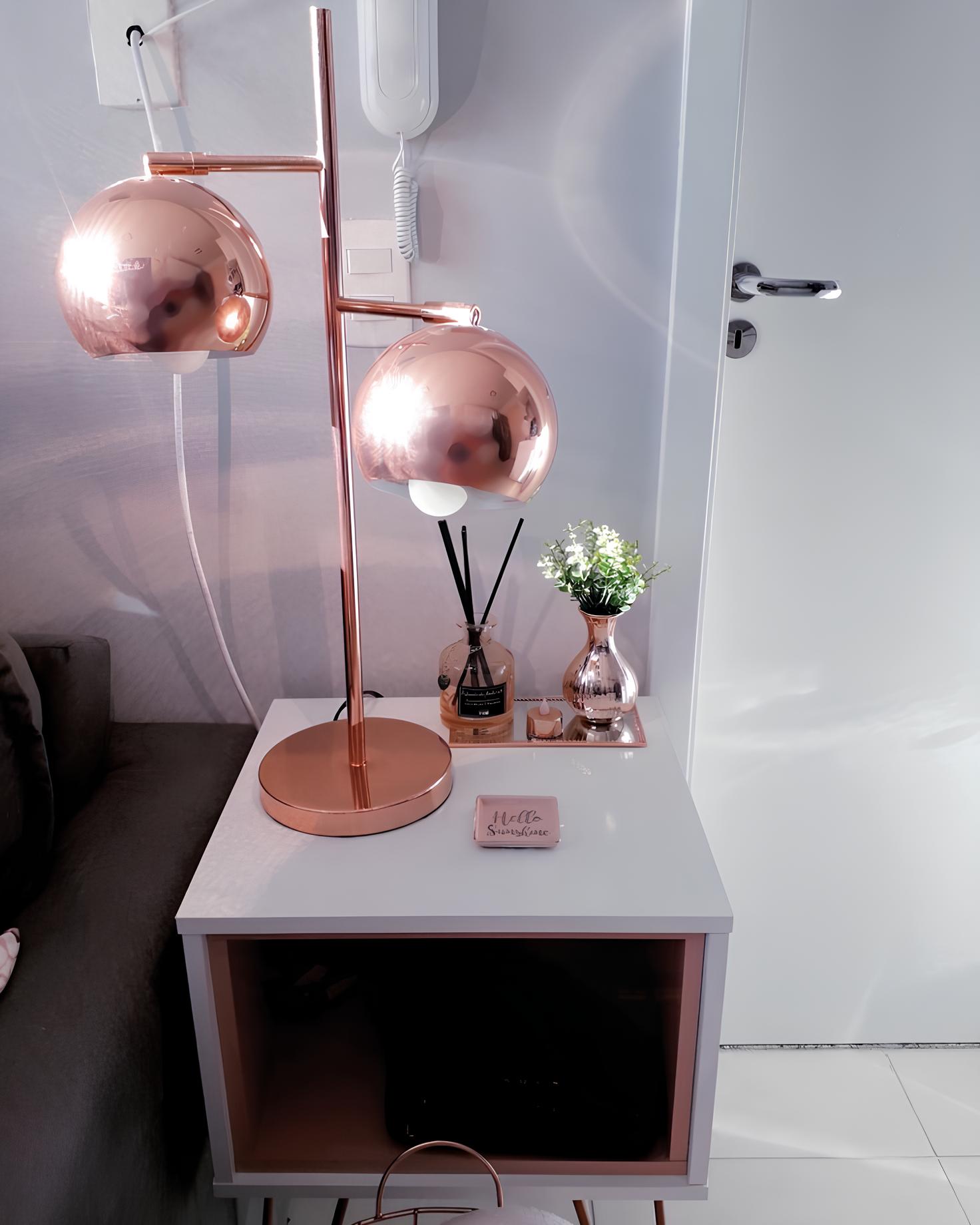 hall de entrada com uma mesinha quadrada de madeira com branco, em cima dela uma luminária moderna na cor rose gold , ao lado da luminária objetos decorativos da mesma cor dela.