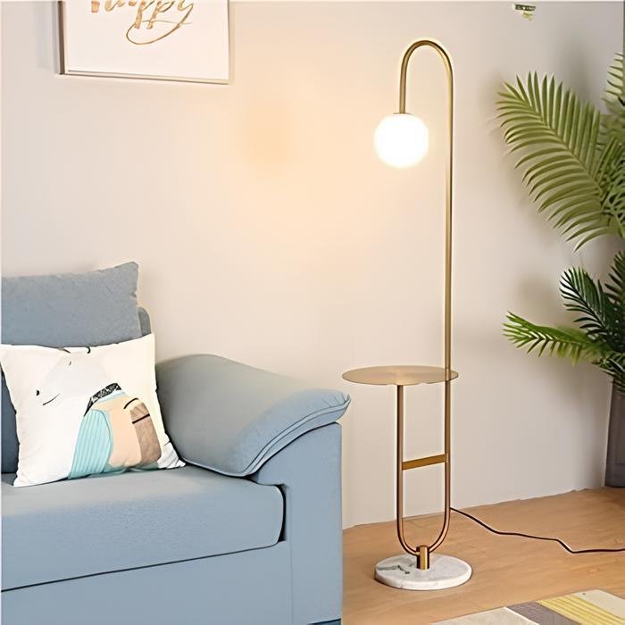 ambiente com um sofá na cor azul claro com uma almofada em cima , ao lado uma luminária de chão alta, ao lado um vaso grande com plantas.