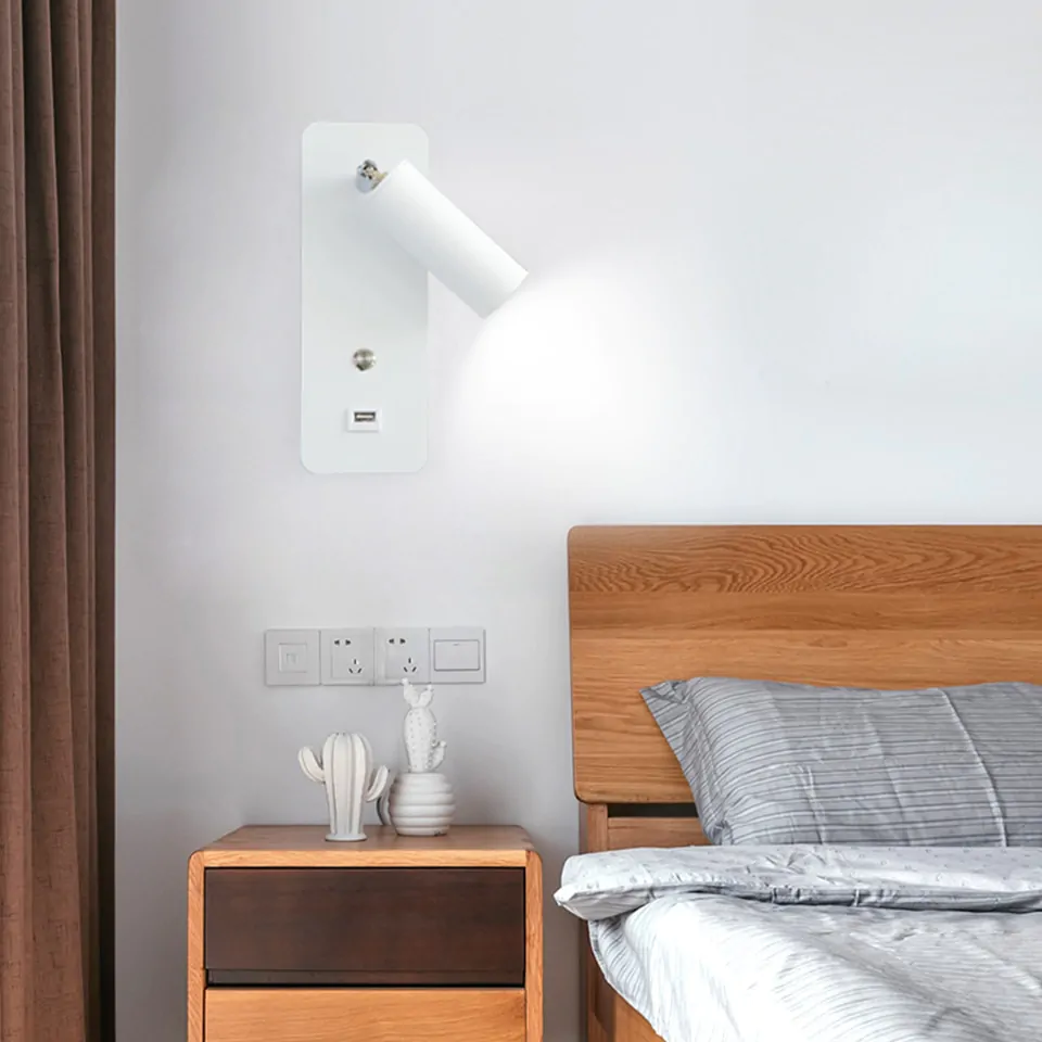 quarto com uma cama de casal com cabeceira de madeira, ao lado um criado mudo de madeira com objetos decorativos em cima, na parede atrás um luminária de parede em estilo spot.