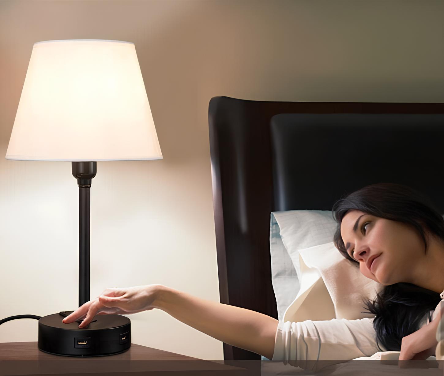 uma moça deitada na sua cama indo desligar uma luminária de touch na cor preta.