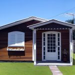 casa de madeira pntada de verniz e branco nas janelas e porta, em volta dela jardim.